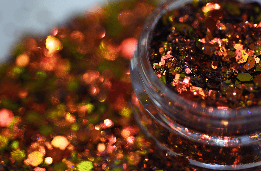Color-shifting loose glitter particles in shades of red, copper, orange, gold, green, and yellow